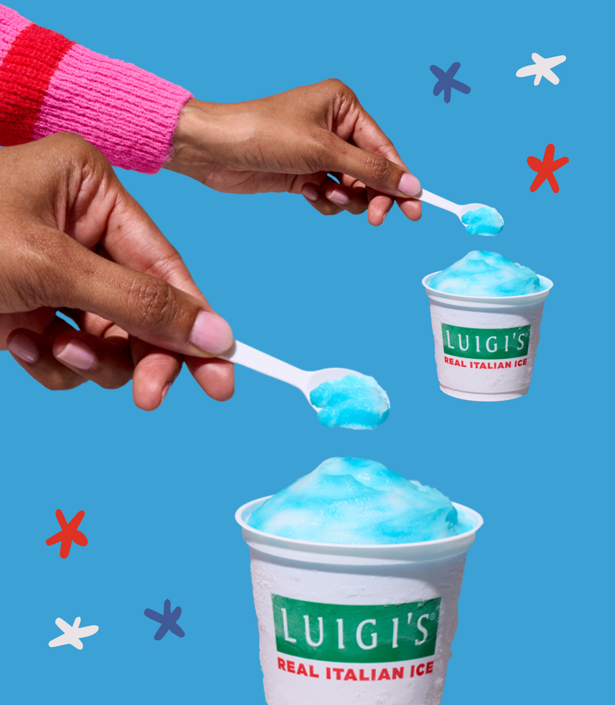 Two hands scooping blue raspberry and lemon swirl LUIGI'S Real Italian Ice. There are two cups, and each hand is holding a white spoon with a scoop of blue Italian ice. Background is blue with red, white, and blue stars.