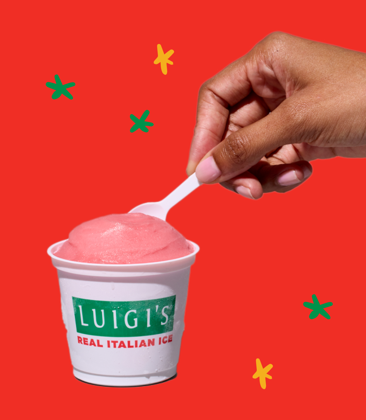 Hand scooping cherry LUIGI'S Real Italian Ice. Background is red with yellow and green stars.