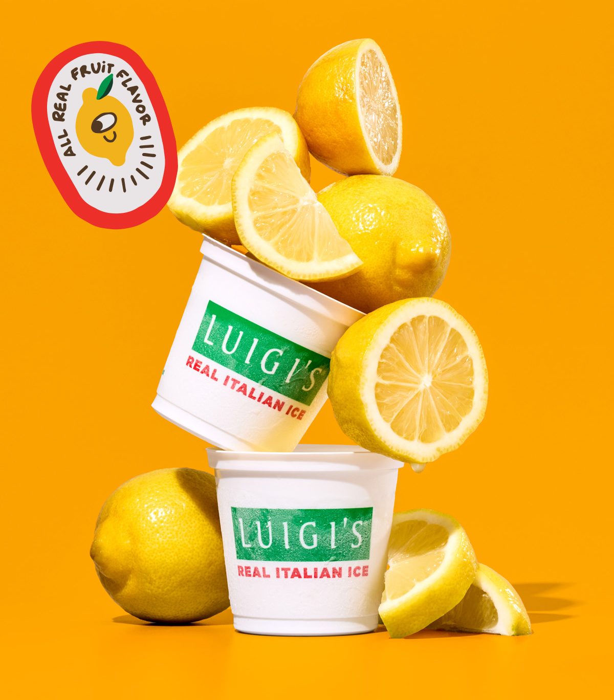 Two cups of lemon LUIGI's Real Italian Ice stacked on top of each other. Lemons are stacked on top of and around the cups. In top left corner, All Real Fruit Flavor sticker with cute lemon graphic. Background is yellow.