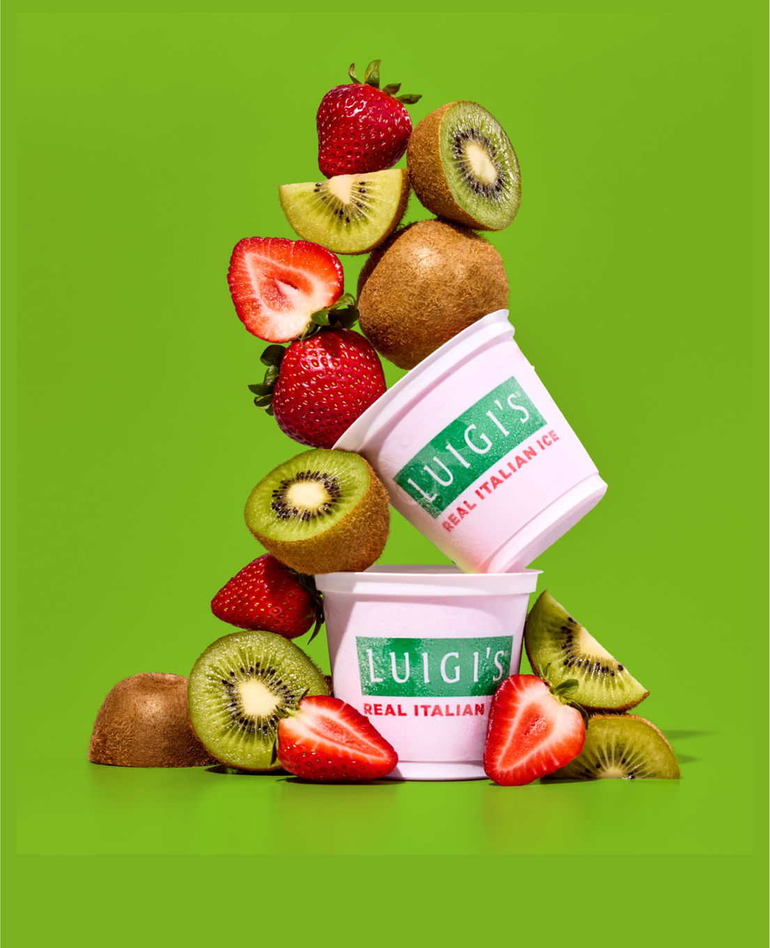Two cups of LUIGI'S real Italian Ice are stacked on each other, while surrounded by kiwis and strawberries. The background is green.