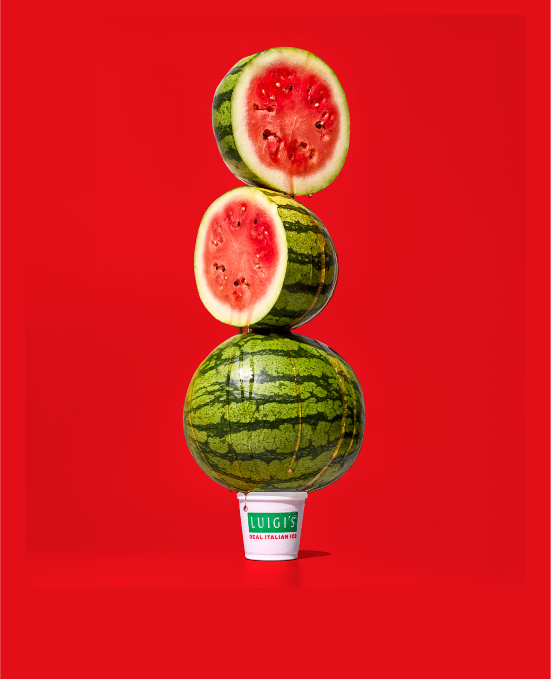 Image of watermelons stacked on top of a cup of LUIGI'S Real Italian Ice. The background is red.